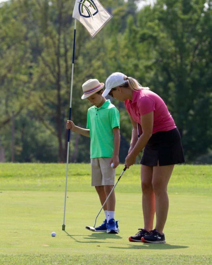mother in putting in the green while son holds flag