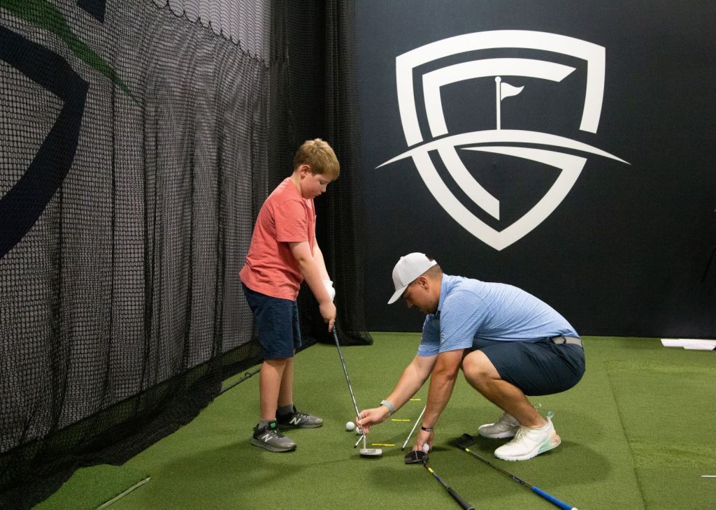 instructor teaching a junior golfer at the indoor facility