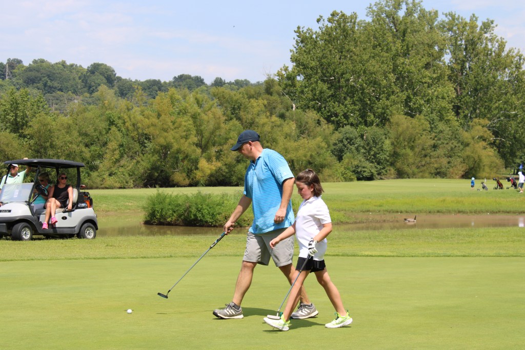 Father and daughter golf players walking across field with golf clubs